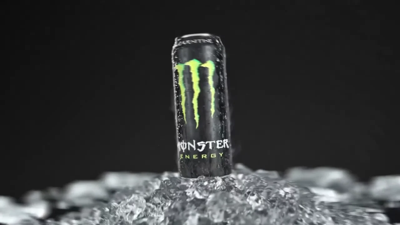 A can of Monster Energy Original standing upright in crushed ice against a black background