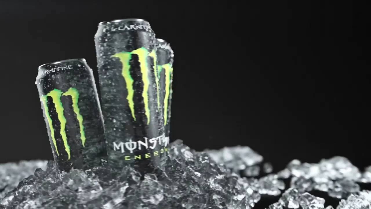 Three cans of Monster Energy Original standing together in crushed ice